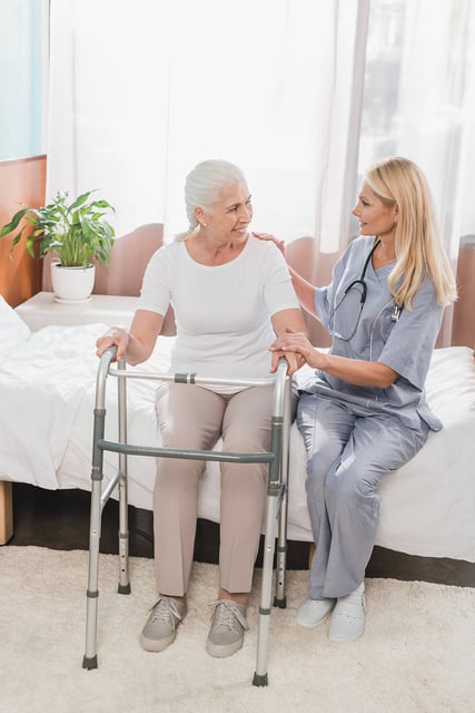 Female nurse assisting an older woman patient stand up using a walker