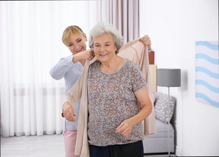 Caregiver helping senior to put sweater on